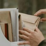 Close-up of hands sorting and organizing documents in a file box outdoors.